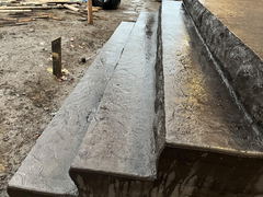 Freshly poured concrete steps with textured surface at a construction site with dirt ground and scattered wooden boards.
