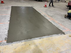 Fresh concrete patch in an indoor warehouse floor with construction cones and workers nearby