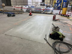 Freshly poured concrete patch on an indoor warehouse floor with construction tools, safety cone, and equipment nearby.