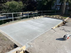 Freshly poured and finished concrete slab driveway section with wood forms and a concrete saw nearby.
