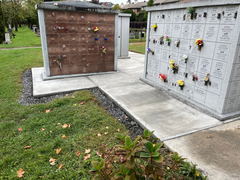 Freshly poured concrete walkway beside cemetery columbaria with engraved niches and flower tributes.