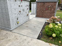 Freshly poured concrete walkway between columbarium walls in a cemetery with hydrangea bushes nearby.