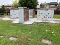 Concrete walkway surrounding three granite columbarium structures with engraved niches and flower memorials in a cemetery setting.