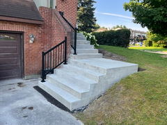 Newly constructed concrete steps with black metal railings leading to the front entrance of a brick house.
