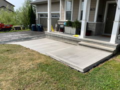 Freshly poured concrete walkway and porch steps next to a residential front porch with grass and driveway visible