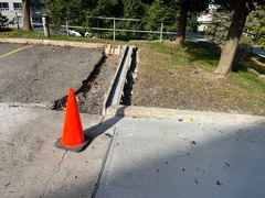 Concrete curb construction with exposed forms next to new sidewalk and a traffic cone marking the edge