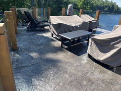 Stamped concrete patio with covered outdoor furniture, glass and wood railing, overlooking a lake