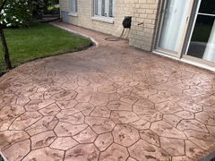 Brown stamped concrete patio with a stone pattern beside a house with sliding glass doors and adjacent green lawn.