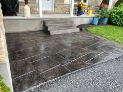 Dark stamped concrete patio with a stone pattern in front of porch steps and landscaped garden.