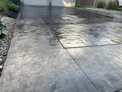 Freshly finished stamped concrete driveway with textured pattern and clean control joints leading to a two-car garage, bordered by decorative rock landscaping.