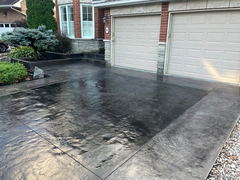 Freshly installed dark stamped concrete driveway in front of a double garage with decorative borders and landscaped garden beds.
