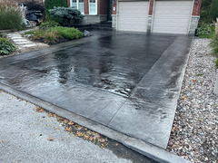 Dark stamped concrete driveway with a decorative border leading to a double garage, bordered by landscaping and river rock.