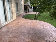 Curved stamped concrete patio next to a brick house with adjacent grass and a tree.