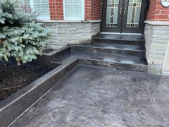 Dark stamped concrete front steps and walkway leading to double entry doors, bordered by stone veneer walls and landscaping.