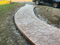 Curved stamped concrete walkway with a stone pattern next to a driveway and parked black SUV