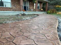 Curved stamped concrete walkway with a stone pattern leading to a brick house front porch