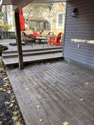 Stamped concrete patio with fallen leaves next to a raised wooden deck with red chairs and a patio table.