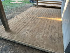 Freshly poured stamped concrete patio with wood plank pattern adjacent to a wooden deck and posts.